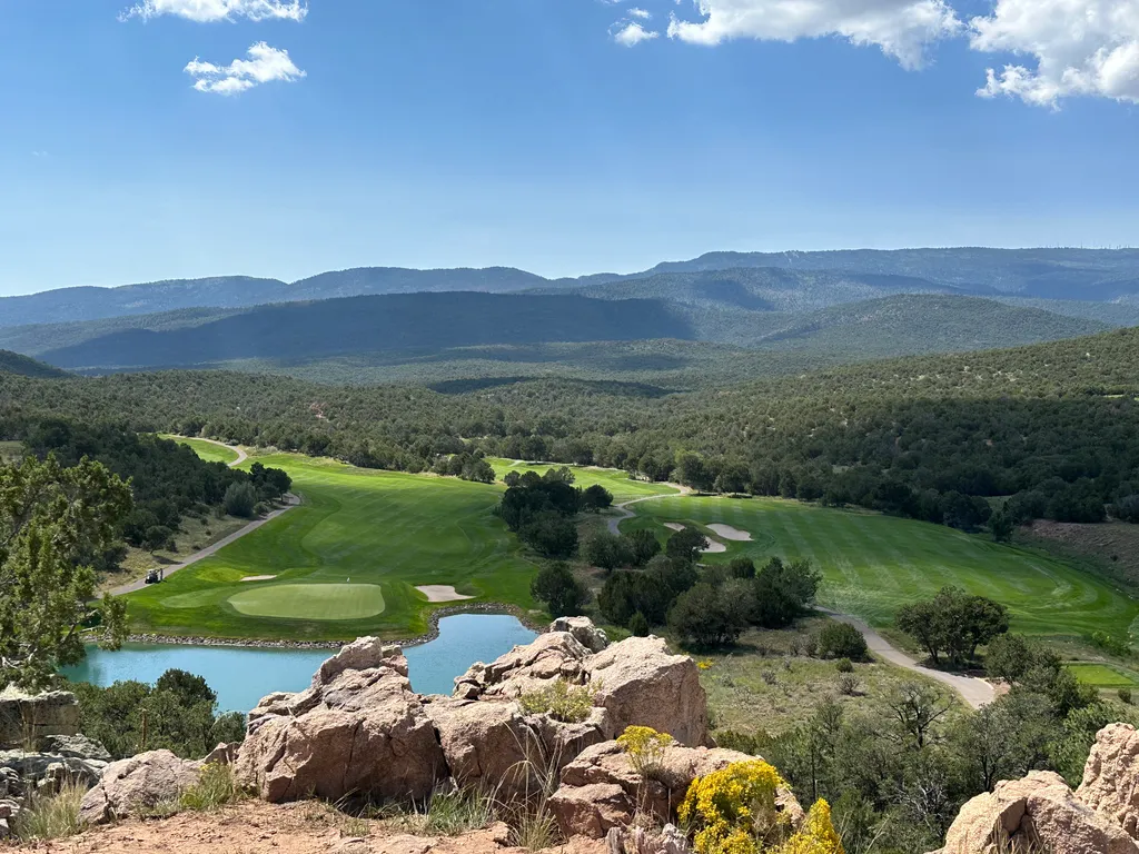 Golf greens and a pond below wooded hills, viewed from a rocky overlook.