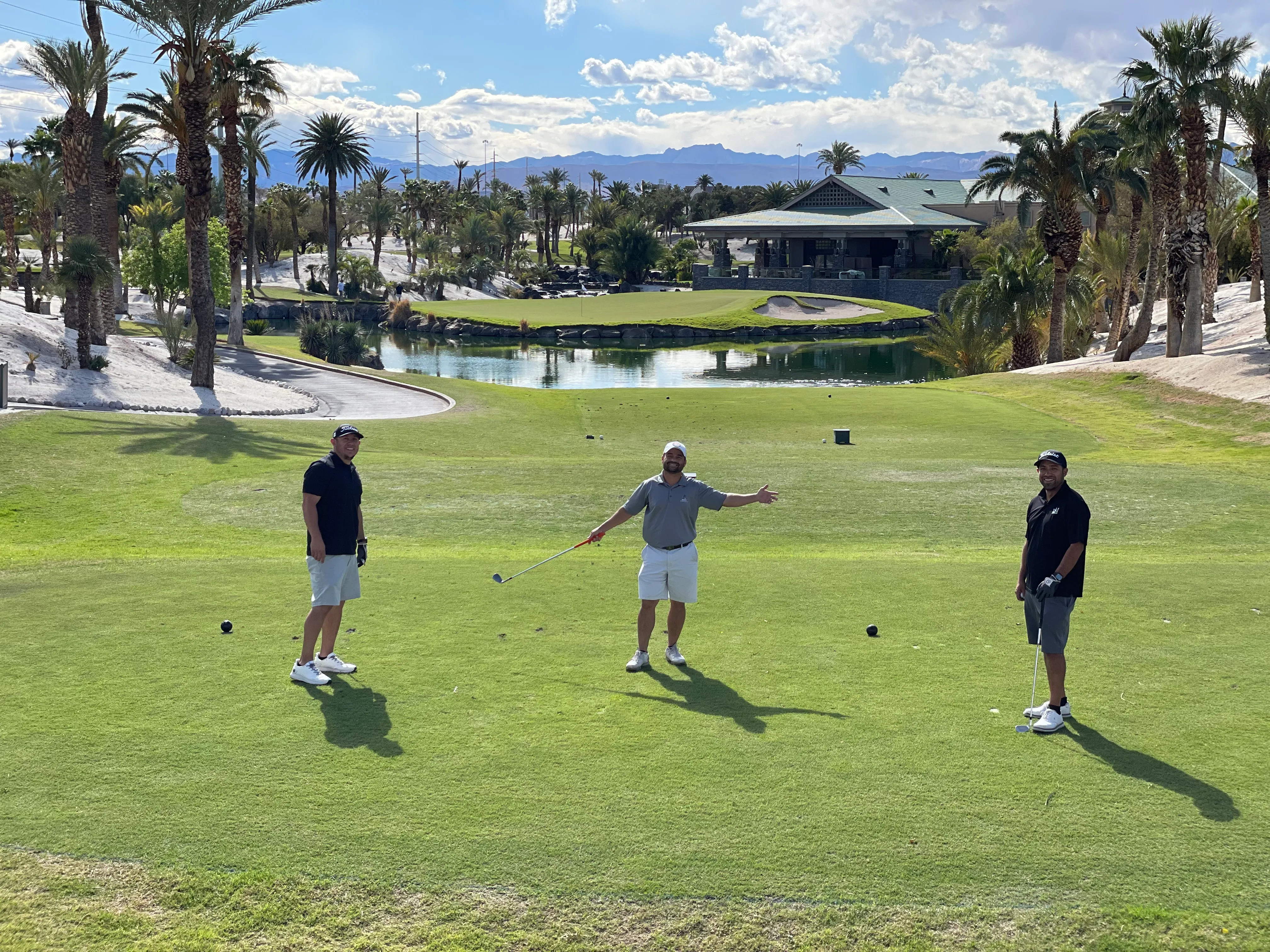 Three golfers on a golf course with palm trees and mountains in the distance.